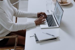 woman typing on laptop with journal and pen beside laptop